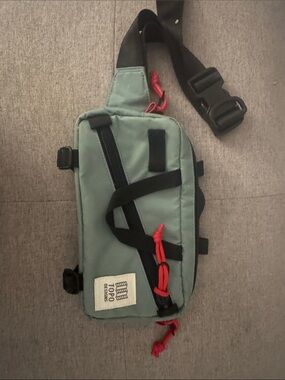 Topo Designs Sage Green Sling Bag with Black Strap and Red Accents